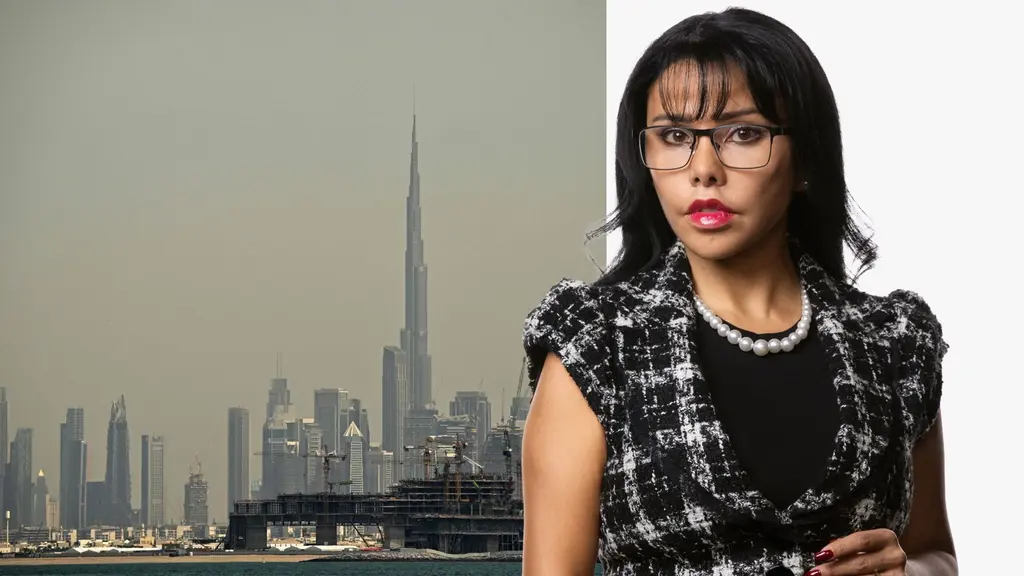 En kvinna i formell klädsel med pärlhalsband står framför en bakgrund som visar Dubai skyline med Burj Khalifa, världens högsta byggnad, synlig mitt i bilden.