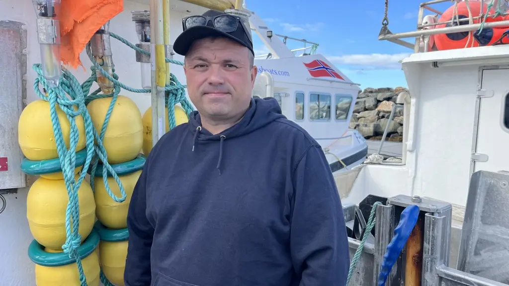 Fiskaren Svein Harald Holmen står på en båt i Vardö, omgiven av gula bojar, rep och fiskeredskap i hamnmiljö.
