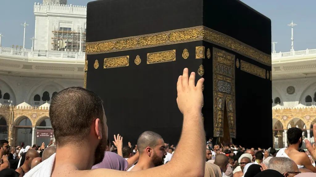 Muslimska pilgrimer samlas runt Kaba, den svarta kubformade byggnaden i Stora moskén i Mecka, Saudiarabien. En person i förgrunden sträcker upp sin hand mot byggnaden.