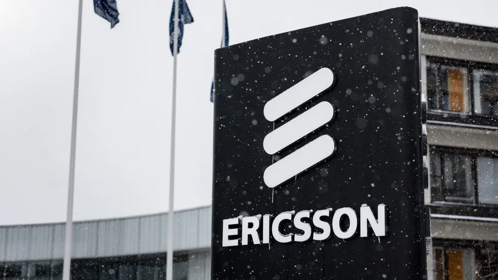 Ericssons huvudkontor i Kista, Stockholm, med en stor skylt som visar företagets logotyp. Byggnaden syns i bakgrunden och flaggor vajar vid sidan. Snöfall täcker platsen.