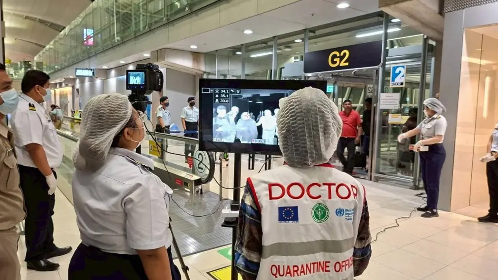 Hälsopersonal övervakar en termisk kamera som skannar resenärer för feber vid Suvarnabhumi flygplats i Thailand. Flygplatsen är fylld med människor, och åtgärder mot Nipah-viruset pågår.