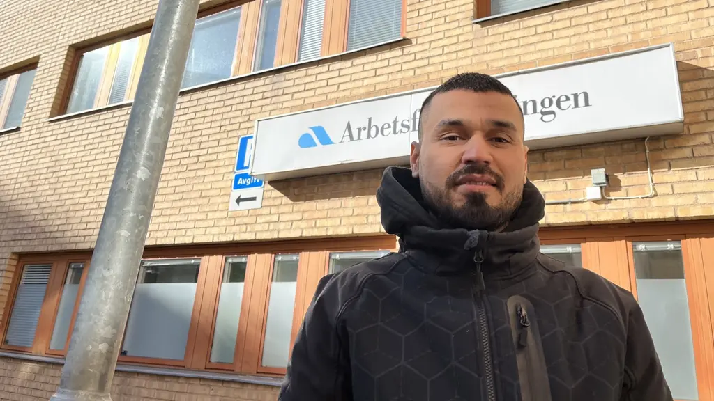 En man står framför en skylt det står Arbetsförmedlingen på.