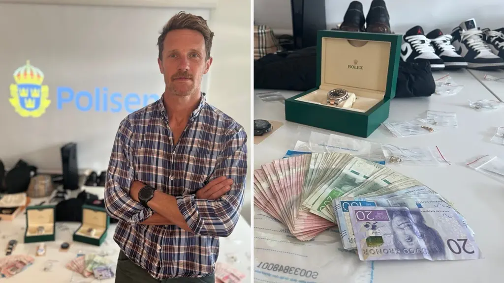 En person står med armarna i kors framför ett bord fyllt med beslagtagna föremål, inklusive kontanter, klockor och skor, i en miljö kopplad till polisens utredning.