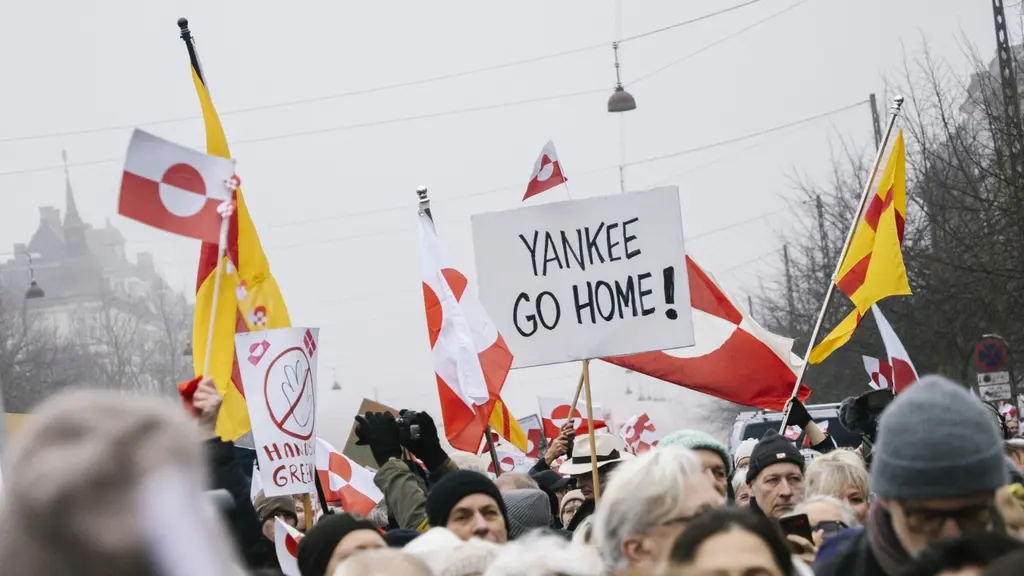 Demonstration i Köpenhamn med deltagare som håller upp skyltar och flaggor, inklusive texten 'Yankee Go Home!' och grönländska flaggor samt gula flaggor med rött kors. Protesten visar stöd för Grönland och dess befolkning.