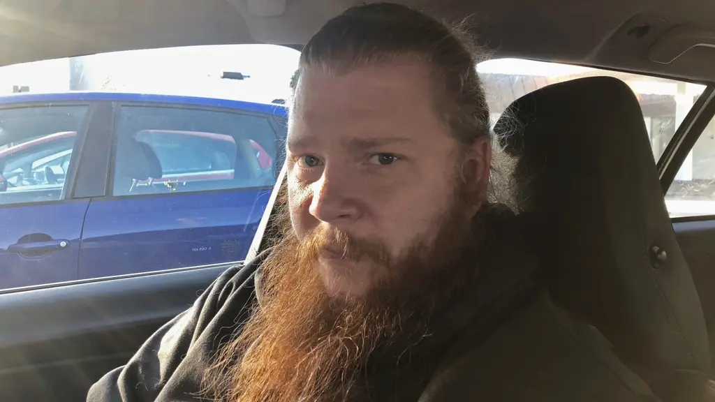 En man sitter i främre passagerarsätet i en bil på en parkeringsplats.