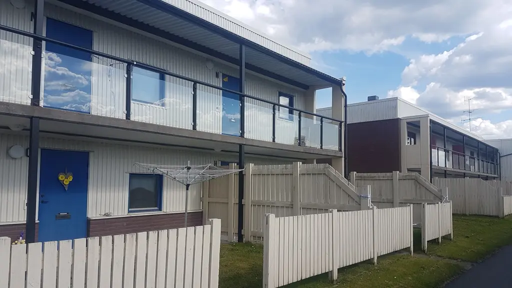 Ett vitt hus med blå dörrar. Vid en av dörrarna skymtar en polisavspärrning.