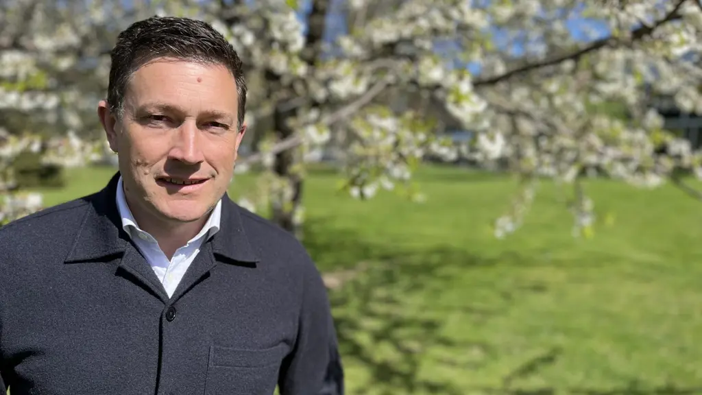 Jimmy Ekström, ordförande för Liberalerna i Jönköpings län, står utomhus framför ett blommande träd med grönt gräs och blå himmel i bakgrunden. Ny partiledare