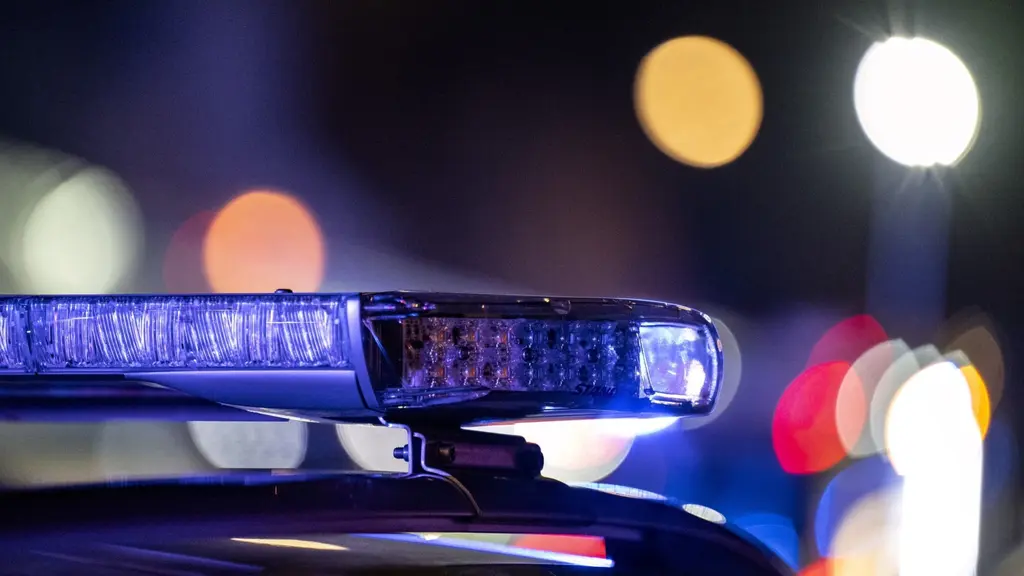 En polisbil med blåljus aktiverade i mörker, med suddiga ljuskällor i bakgrunden. Bilden illustrerar en insats under kvällstid.