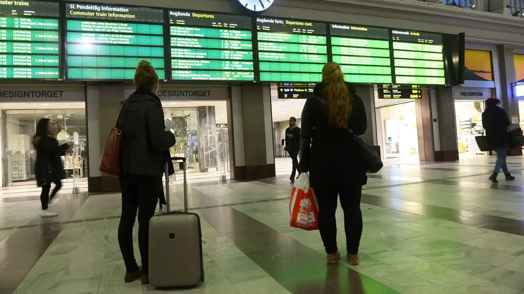 Två kvinnor tittar på informationsskyltar om avgångar på en tågstation.