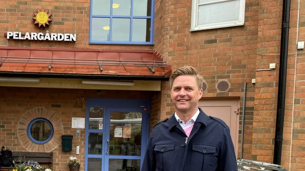 Christian Holm framför entrén till Pelargården, ett tegelhus med blå dörr och fönster. Politikerbesök vid vård- och omsorgsboende.