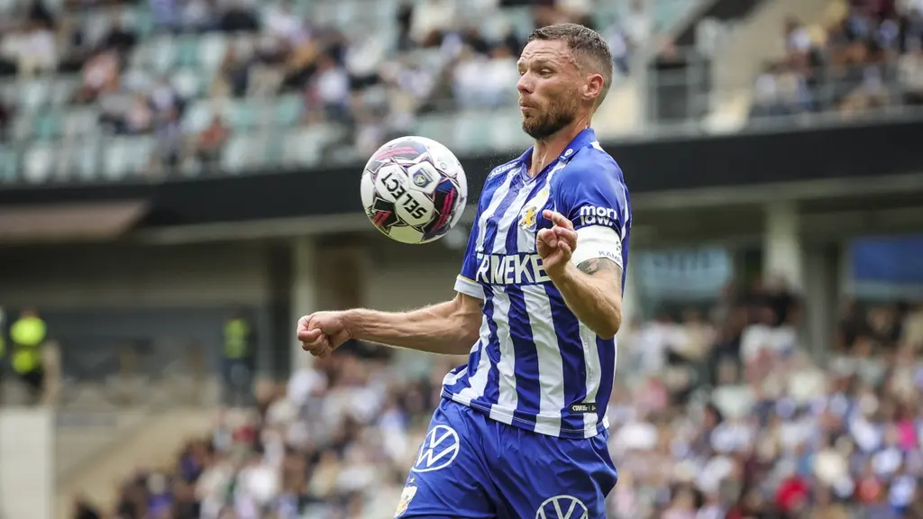 Manlig fotbollsspelare i blåvitrandig tröja tar emot boll med bröstet.