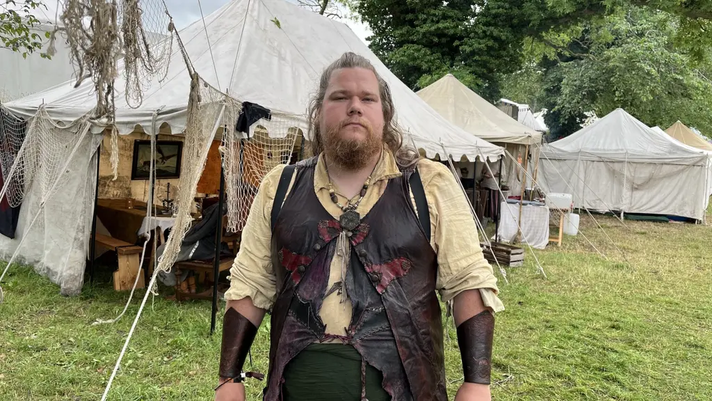 Jonatan Stjernlöf står klädd i piratinspirerade kläder framför vita tält på en gräsplan.