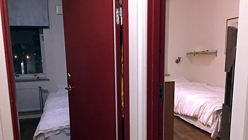 På bilden ser man in genom två dörrar till två rum på ett vandrarhem. Man ser två sängar och skymtar en våningssäng. I de två rummen bor en hemlös familj med fyra barn. Foto: Anna Bubenko/Sveriges Radio. 