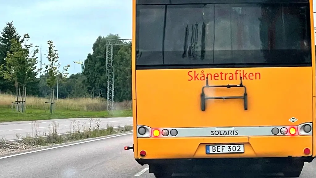 En gul regionbuss från Skånetrafiken står på en landsväg. Busshållplats och omgivande grönska syns i bakgrunden. 