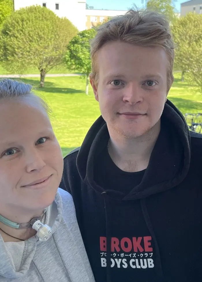 Vendela och Pontus står tätt intill varandra i en dörröppning, med grön gård och cyklar i bakgrunden. Bild till nyhet om epilepsianfall i butik i Mariestad.