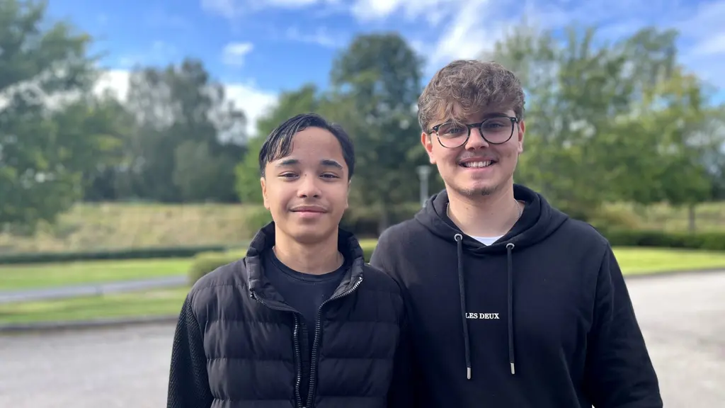 Två killar står i svart jacka och svart tröja. De tittar in mot kameran.