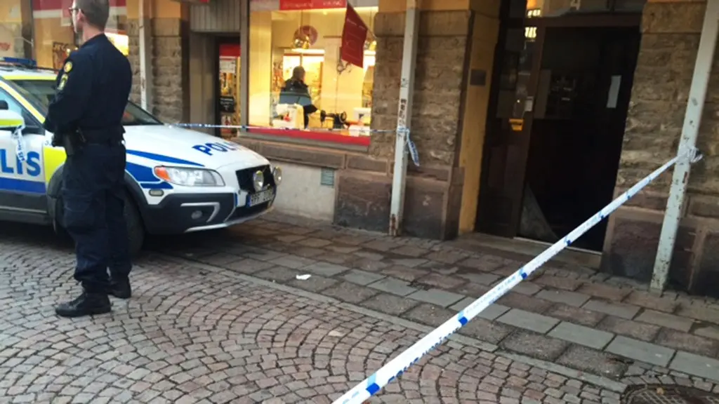 Avspärrningsband utanför trappuppgång, polisbil och en polis. 