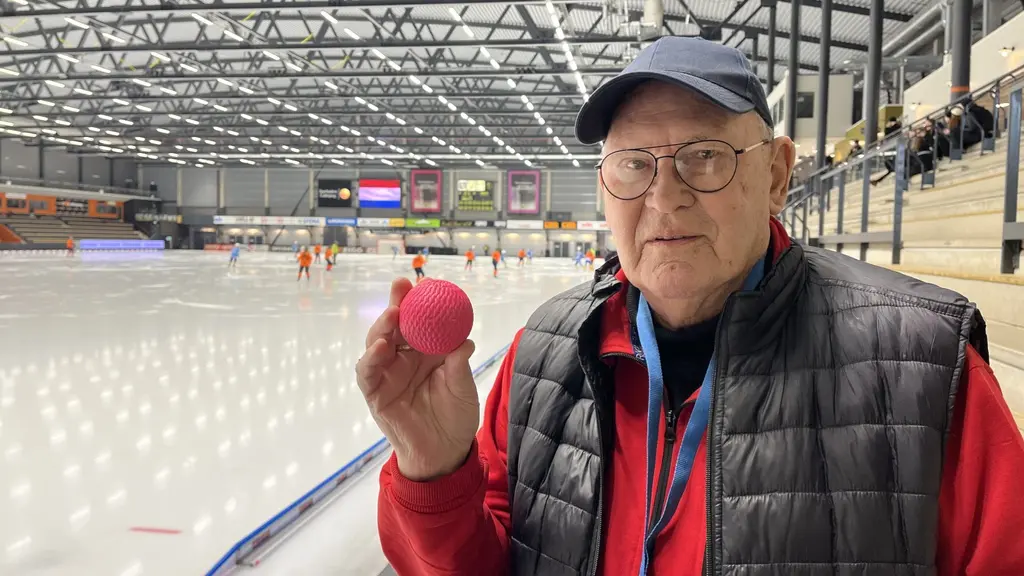 En man med keps håller i en rosa bandyboll vid isen.