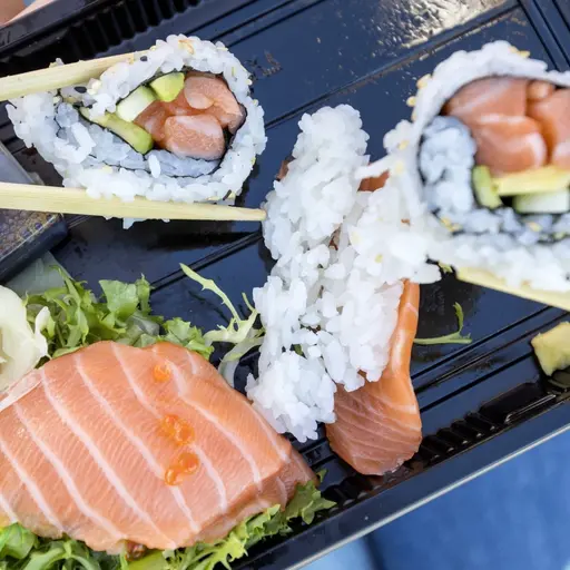 Två ungdomar äter sushi ur en plastlåda med laxnigiri, makirullar och ingefära – genrebild till nyhet om restaurang och misstänkt magsjuka i Tidaholm.