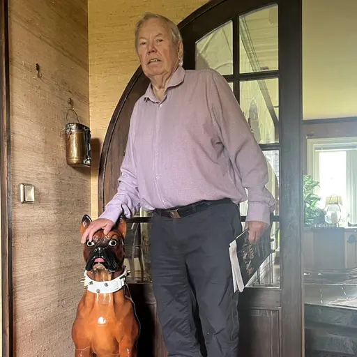 En man med skjorta står bredvid en porslinshund inne i ett hus.