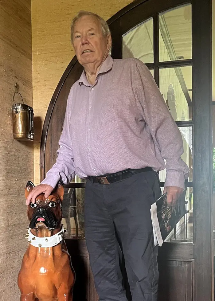 En man med skjorta står bredvid en porslinshund inne i ett hus.