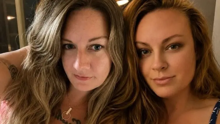 Caroline och Maria efter misstänkt matförgiftning av sushi i Tidaholm. Två kvinnor sitter tätt intill varandra inomhus, ansiktena maskerade.