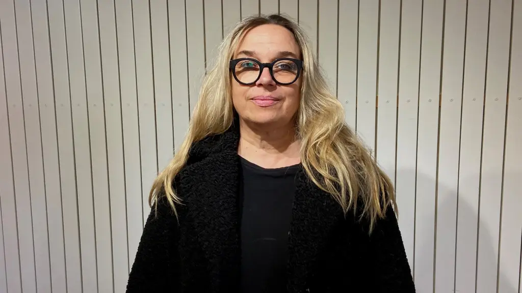 Annika Fredriksson, vd för Swedish Lapland, står framför en vit vägg med träpaneler. Hon har långt blont hår, svart tröja och en svart kappa. Bilden är tagen inomhus.