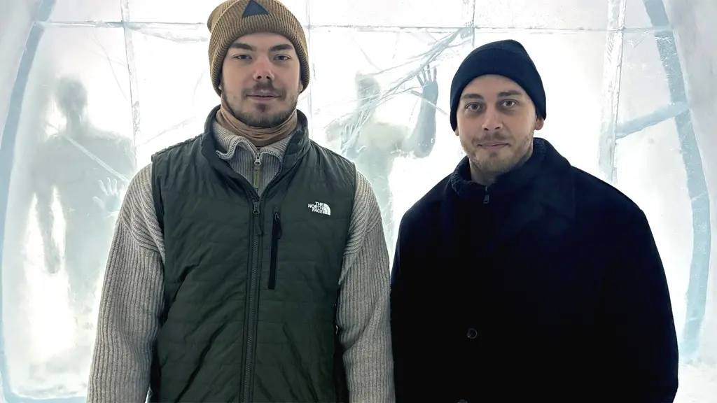 Kreatörerna Charlie Hammarlund och Robin Lind står framför ett konstverk av is med suddiga konturer av människoliknande figurer i bakgrunden.