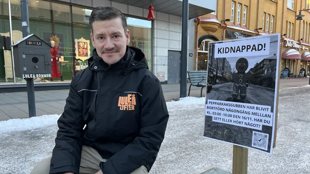 Centrumutvecklaren Jimmy Renlund sitter utomhus bredvid en skylt med texten 'Kidnappad!' som efterlyser en försvunnen pepparkaksgubbe. Bakgrunden visar en stadsmiljö med byggnader och snö.