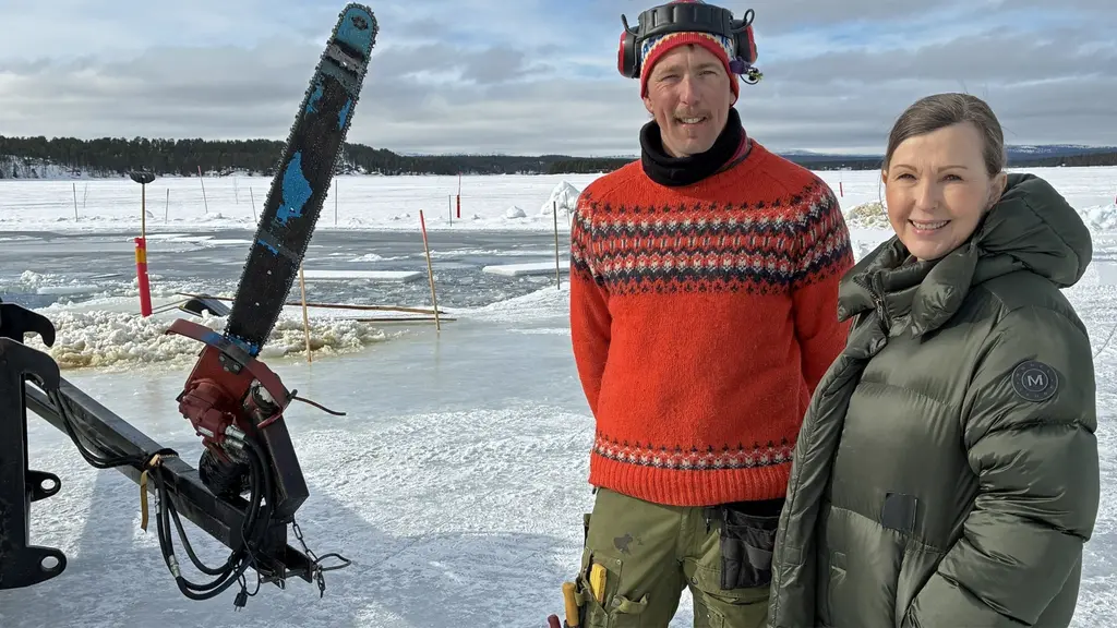 Två personer står på Torneälven. En stor motorsåg och området för isskörden syns i bakgrunden, omgivet av ett snöklätt landskap och en klar himmel.