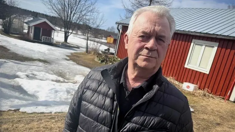 Sven-Erik Bucht i mörk täckjacka på sin gård utanför Haparanda, med röda byggnader och en del snö på marken.