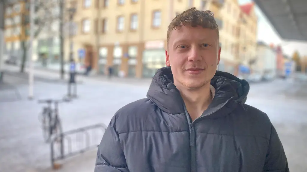 En man med kort blont hår och mörk dunjacka står i en utemiljö