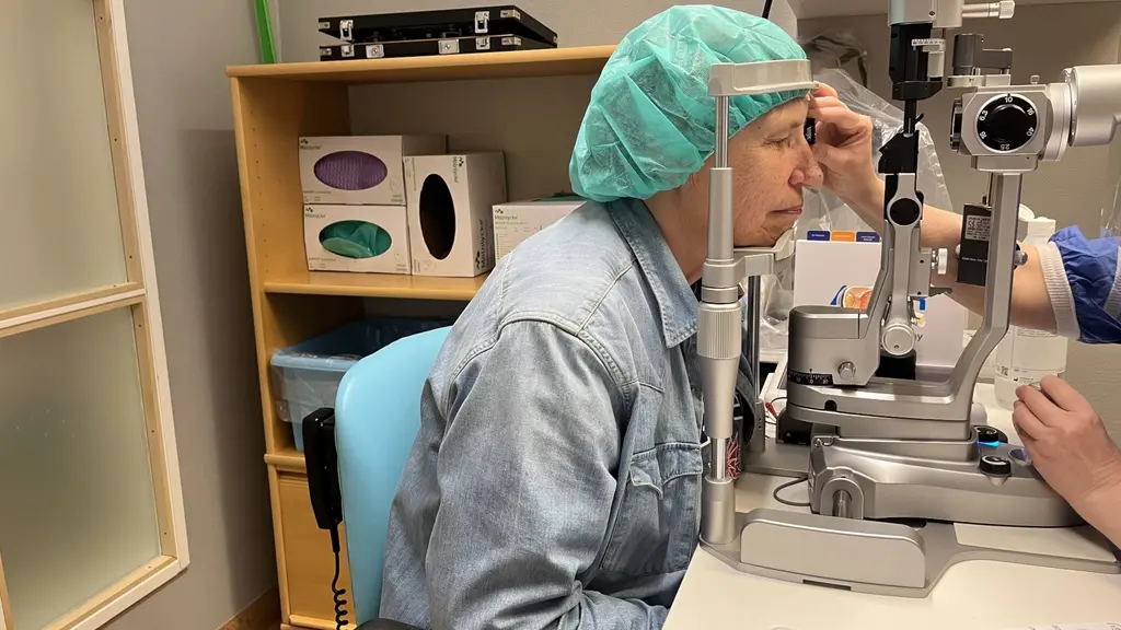 En patient sitter mittemot en läkare och får sina ögon undersökta. Patienten har operationskläder. 