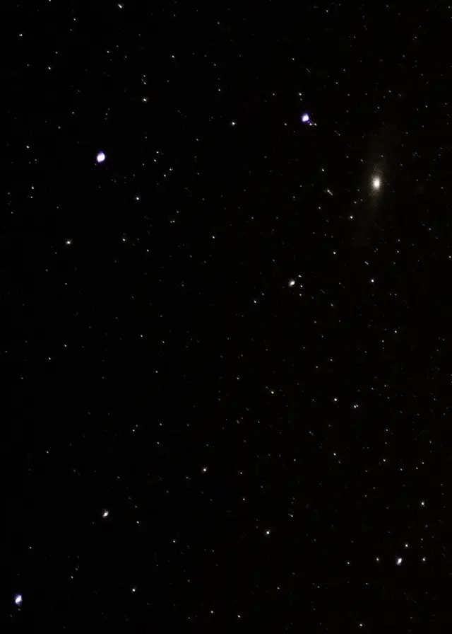 Mörk natthimmel med stjärnor utspridda och Andromedagalaxen synlig som en ljusare fläck i mitten av bilden. En gul streckad linje löper horisontellt genom bilden.