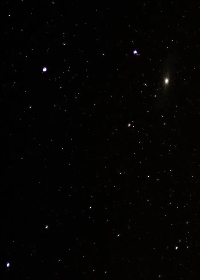 Mörk natthimmel med stjärnor utspridda och Andromedagalaxen synlig som en ljusare fläck i mitten av bilden. En gul streckad linje löper horisontellt genom bilden.