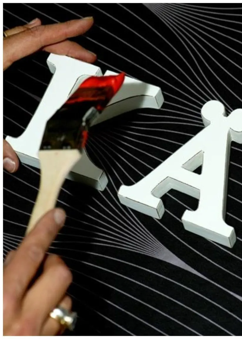 Till höger vita bokstäver som målas röda och bildar ordet ”kär”. Till vänster en kvinna med kort hår.