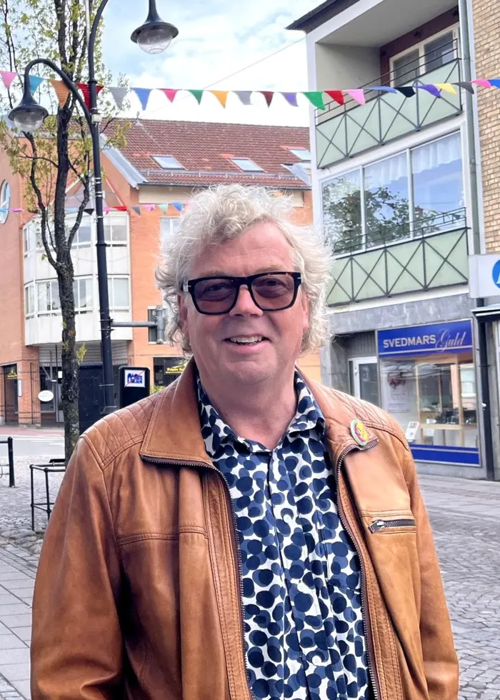 En man med solglasögon står på en gata i en stan.