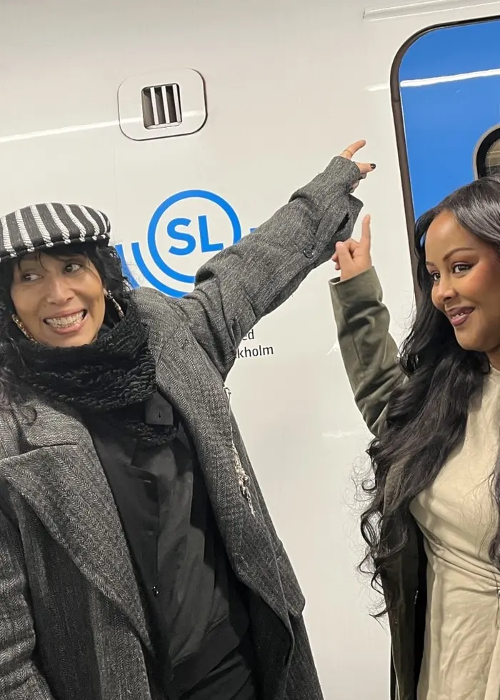 Titiyo och Cherrie poserar framför en tunnelbanevagn på Stockholms röda linje, som är dekorerad med namnen på artister med koppling till Stockholm. En SL-logotyp är synlig på vagnen.