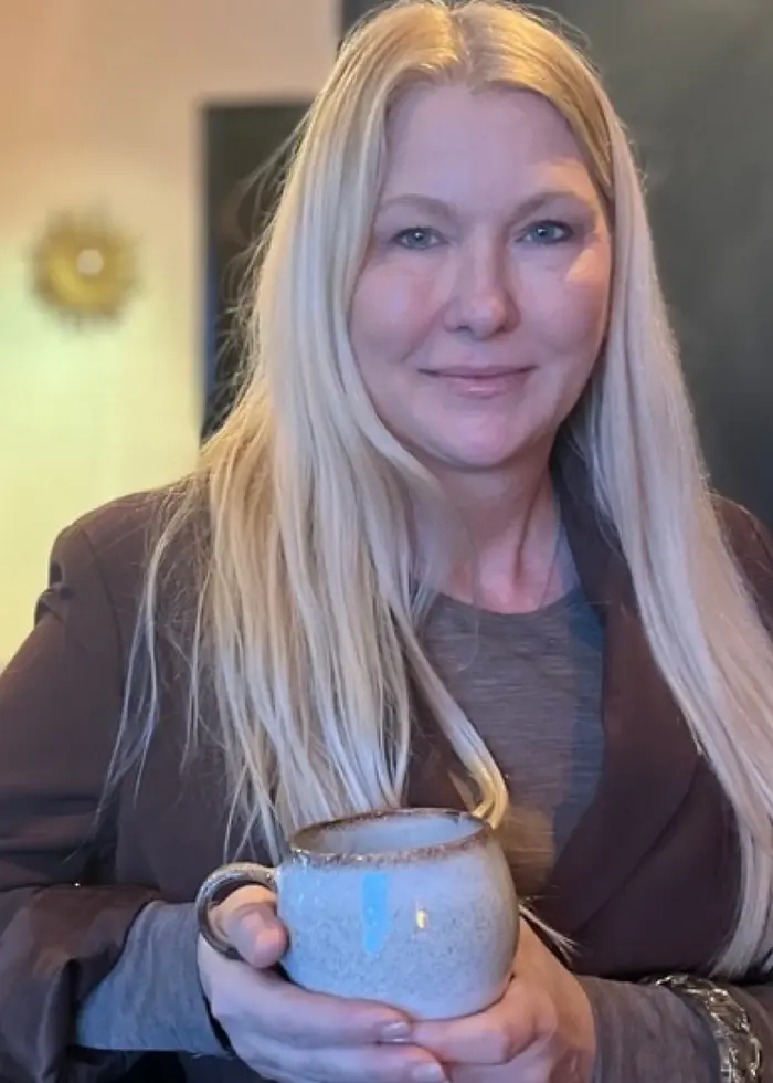 Paulina Lundström, som har långt blont hår, står i ett kök och håller en kopp i händerna.