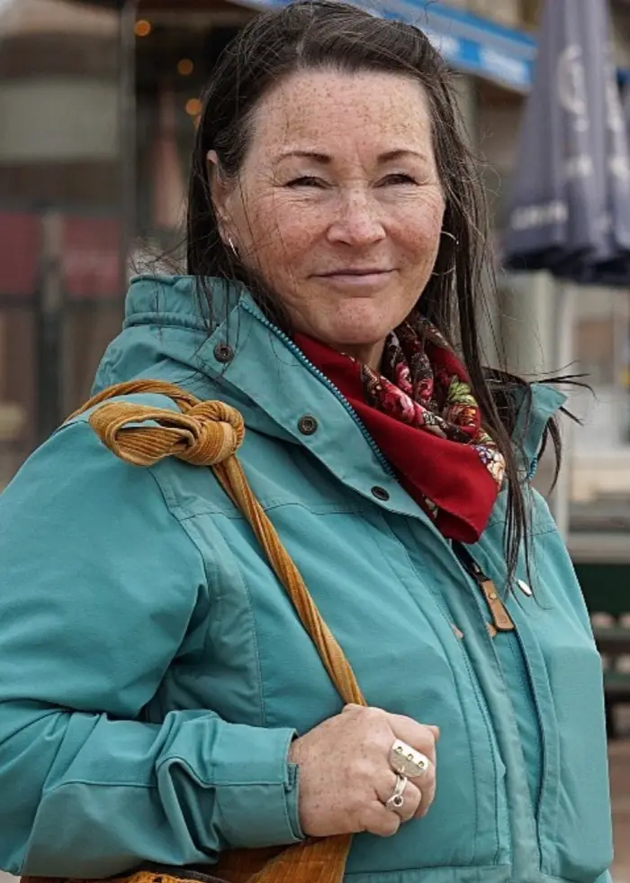 Två kvinnor står separat i en bildsplitt. Den vänstra personen bär en turkos jacka och har en flätad frisyr, medan den högra personen bär en mörk jacka och en rutig halsduk. Bakgrunden visar stadsmiljö och snölandskap.