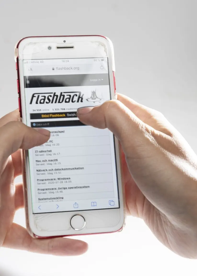 En kvinna håller i en smartphone och scrollar på internettforumet Flashback. Telefonens skärm visar text och rubriker. Bakgrunden är ljus och suddig, med fokus på händerna och skärmen.