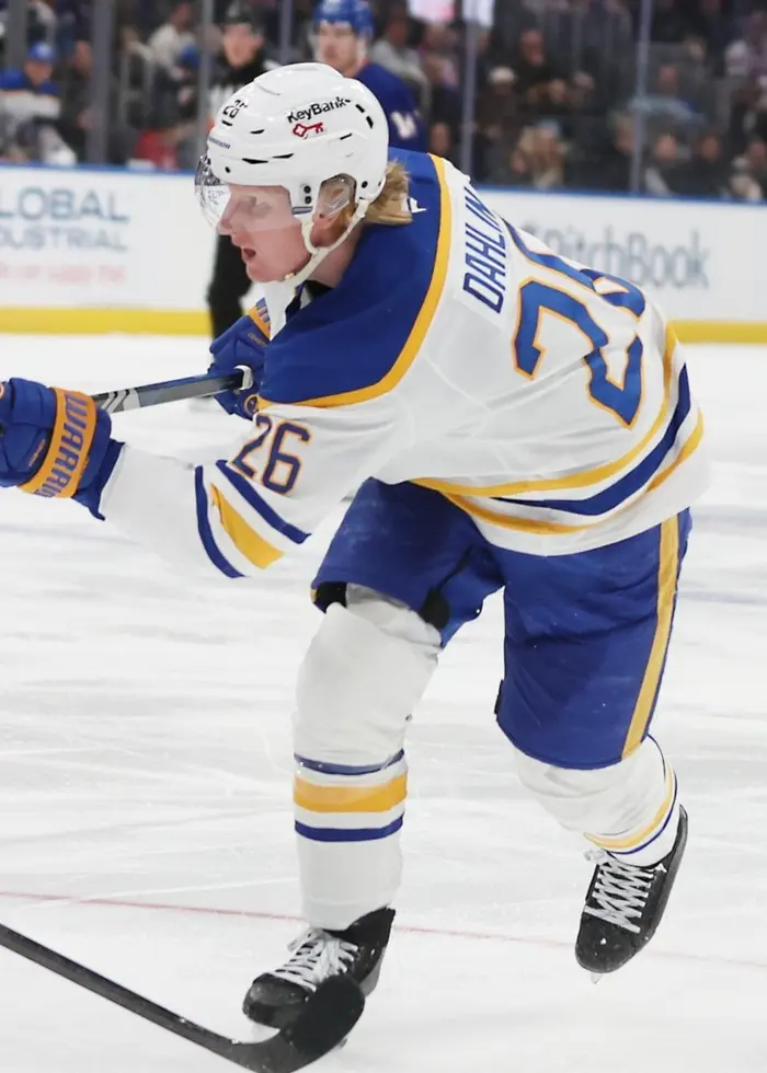 Två hockeyspelare på isen. En med vit tröja och en med blå tröja. Den med vit tröja tar ett avslut.