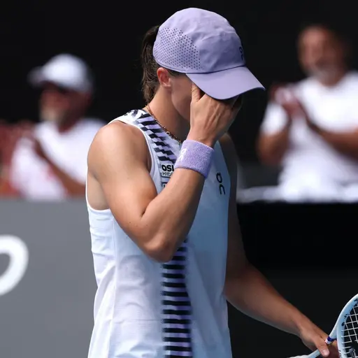 En tennisspelare med keps och vit ärmlös topp håller ena handen över ansiktet och den andra handen på racketen. I bakgrunden syns publik i oskarpt fokus. Bilden är från Australian Open.