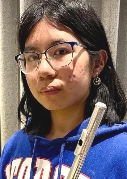 Ruiqi Zhou står framför beige gardiner iklädd en blå tröja med text. Hon håller en silverfärgad flöjt i handen.