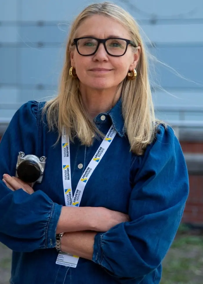 Till vänster syns en person i blå skjorta och halsband som står framför en byggnad, och till höger en rallybil som kör snabbt genom ett snöigt landskap med skog i bakgrunden.