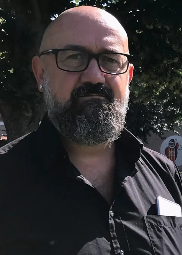 Till vänster syns en person som står utomhus framför ett träd, klädd i en mörk skjorta. Till höger ligger förpackningar med glass på ett vitt bord, en liten kartong och en större plastbehållare.