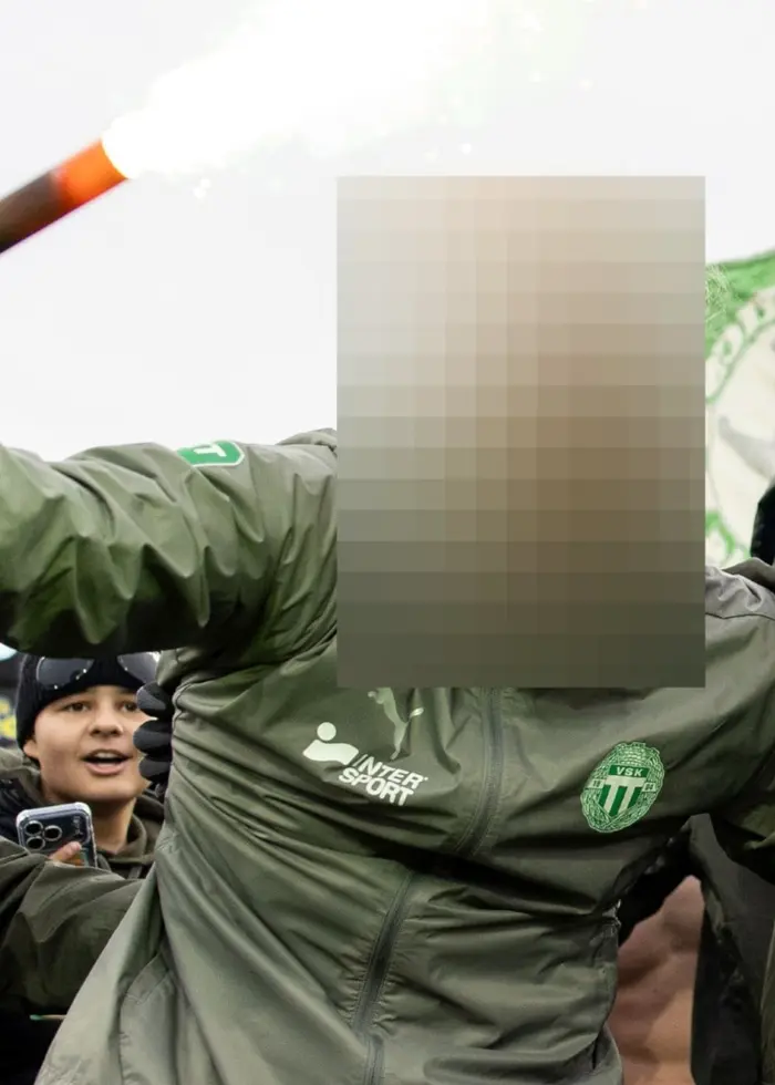 Personer klädda i VSK-kläder håller upp en bengalisk eld på en fotbollsplan. En grön flagga syns i bakgrunden.