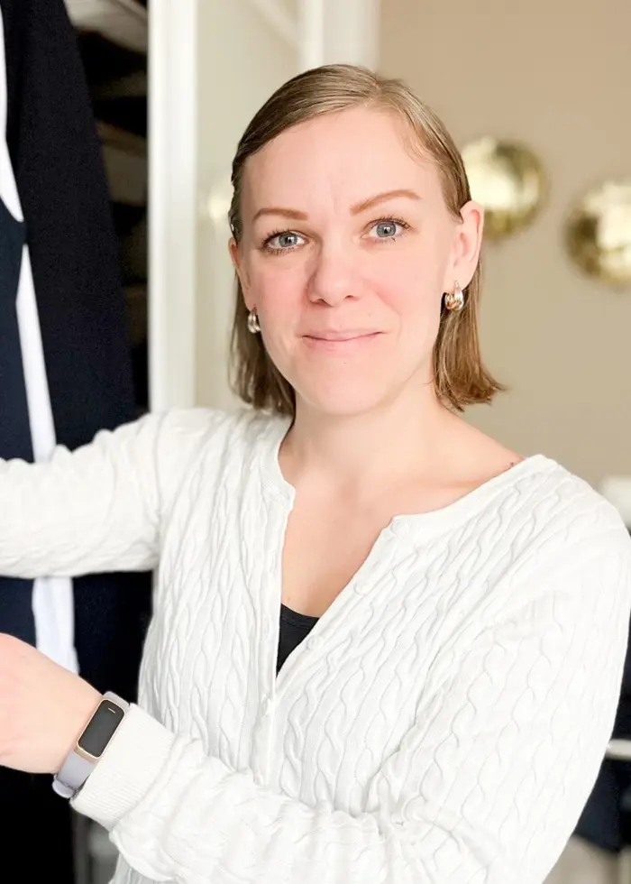 En person klädd i vit tröja står framför en garderob och tittar på kläder, inklusive en leopardmönstrad jacka och rutiga plagg. Bakgrunden visar en ljus inomhusmiljö med väggdekorationer.