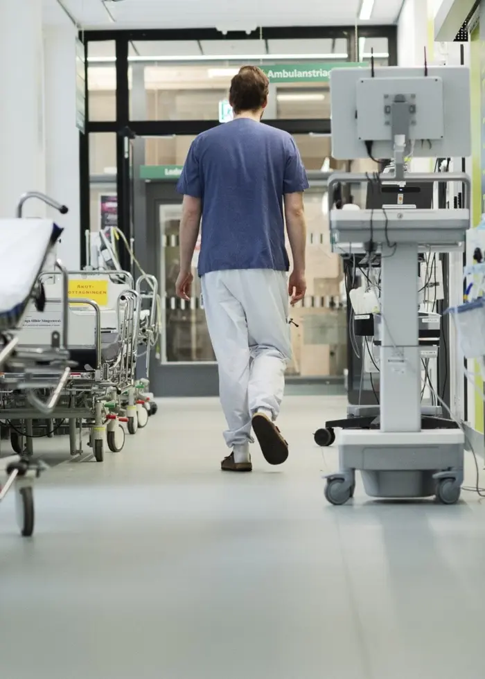 En person i sjukvårdskläder går genom en ljus korridor på en akutmottagning. Sängar och medicinsk utrustning står längs väggarna. Bilden är tagen på Danderyds sjukhus i Stockholm.