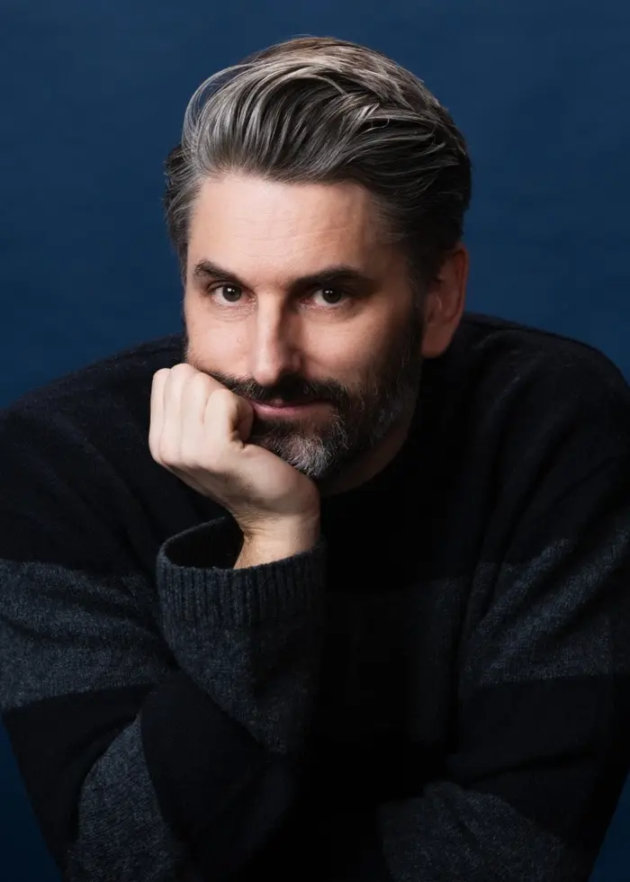 Portättfoto på förfataren Andrev Walden som lutar huvudetmöt höger hand och tittar in i kameran.